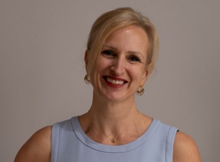 Dr-Magdalena-M-Oledzka. Smiling woman with short blonde hair wearing a light blue sleeveless top against a gray studio background.