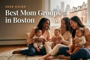 Three diverse moms holding their babies at a welcoming mom group meetup in Boston, with the Boston skyline and brownstones in warm daylight behind them, illustrating a guide to the best mom groups in Boston for 2026
