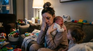 An overwhelmed mom sitting on the floor holding her baby, illustrating struggling mom quotes for the hard days.