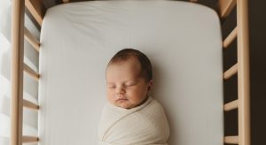 A newborn sleeping calmly on their back in a bare safe bassinet