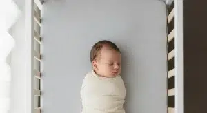 Content newborn resting on their back in a bare bassinet with a fitted sheet only