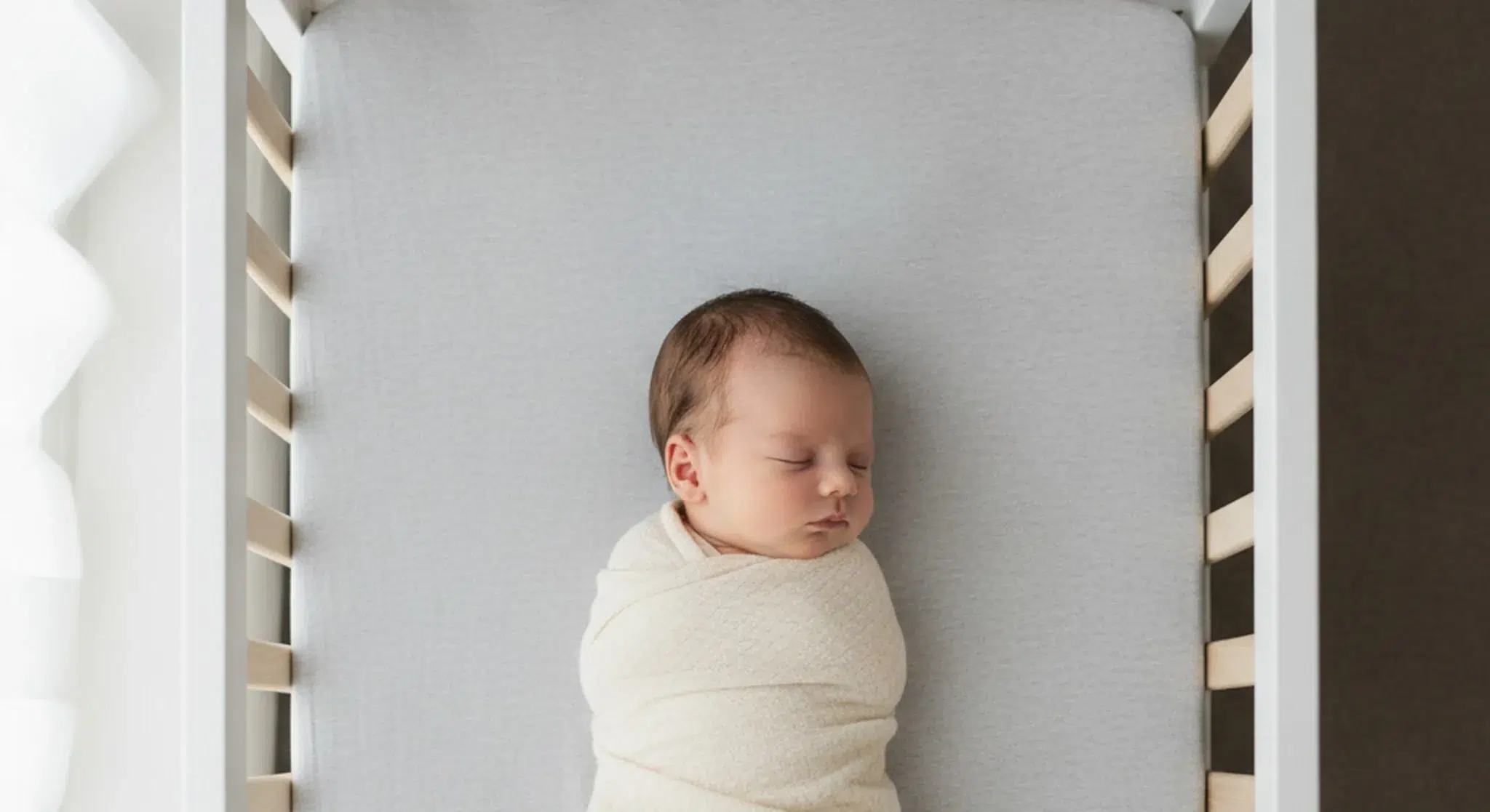 Content newborn resting on their back in a bare bassinet with a fitted sheet only