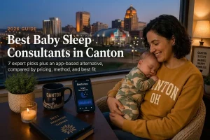 Mother holding a sleeping baby by a window over Canton's downtown evening skyline, baby sleep consultants in Canton.