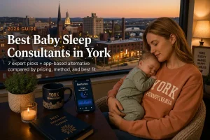 Tired York Pennsylvania mother holding her sleeping baby by a window at dusk, researching the best baby sleep consultants in York