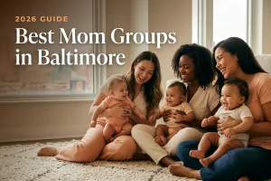 Three diverse moms holding their babies at a welcoming mom group meetup in Baltimore, with the Baltimore Inner Harbor skyline in warm daylight behind them, illustrating a guide to the best mom groups in Baltimore for 2026