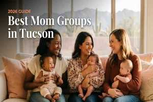 Four moms sit on a couch with their babies, smiling and chatting by a sunlit window. Overlay text reads ‘2026 GUIDE Best Mom Groups in Tucson.’