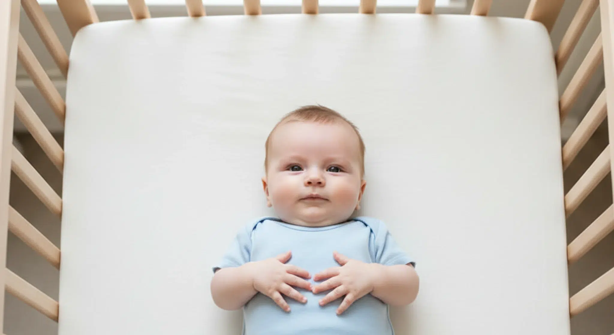 Awake baby resting on their back in a bare safe crib