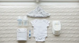 Neatly arranged baby registry essentials including bottles, onesies, diapers and a swaddle on a table