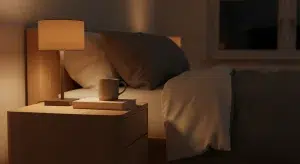 Open book and a warm mug on a bedside table beside a softly lit lamp at night
