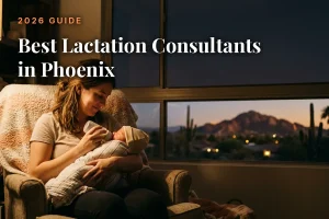 Mother feeding her baby by an evening window with the Phoenix skyline, cover image for the best lactation consultants in Phoenix guide