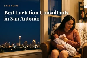Mother holding a swaddled newborn on her lap at home by a window with city lights outside; overlay reads 'Best Lactation Consultants in San Antonio' (2026 Guide).