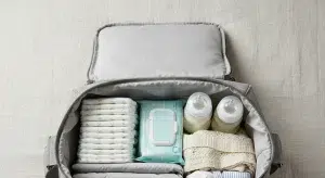 Open diaper bag on a bed with diapers, wipes, bottles, and baby clothes neatly arranged