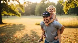 Dad wearing a Girl Dad hat giving his daughter a piggyback ride in a park