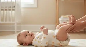 Baby lying on a soft mat, caregiver gently lifting and holding their feet in a bright nursery setting.