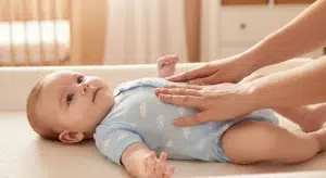 Parent gently massaging an awake baby's tummy in slow circular motions on a padded changing mat
