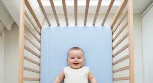 Baby smiling while lying on a blue mat inside a wooden playpen.