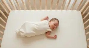 Newborn sleeping on their back in a bare crib with head turned to the side