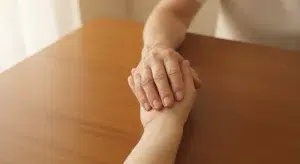 Two hands resting together on a wooden table in soft daylight
