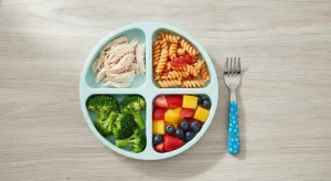 Colorful balanced toddler dinner plate with soft chicken, pasta, broccoli and fruit in small pieces