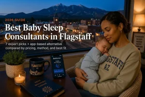 Mother holding a sleeping baby by a window overlooking the Flagstaff skyline at dusk with pines, guide to baby sleep consultants in Flagstaff