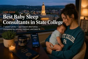 Mother holding a sleeping baby by a window overlooking the State College skyline at dusk, guide to baby sleep consultants in State College