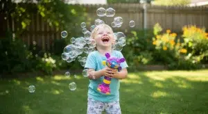 A laughing child playing with a bubble toy outdoors surrounded by floating bubbles in a sunny backyard