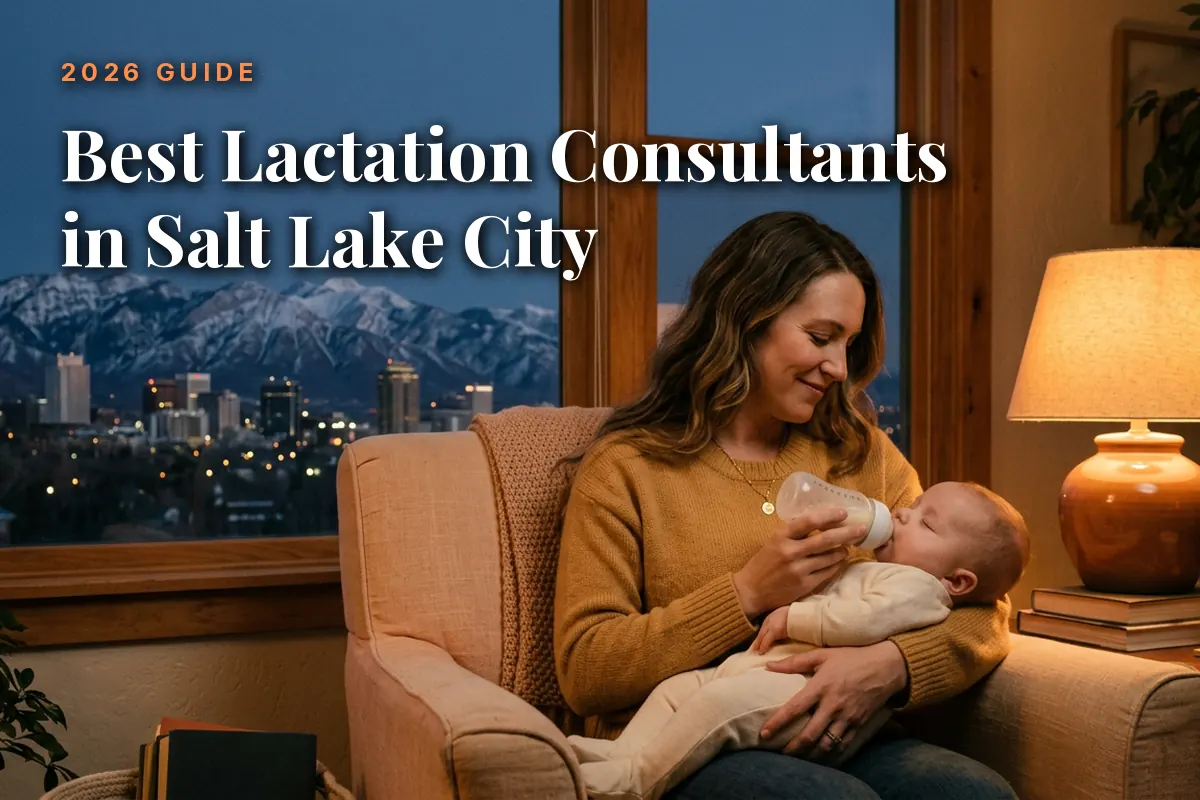 Woman bottle-feeds a baby on a sofa in a cozy living room, with city lights and snowy mountains visible through a large window behind them.