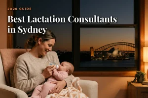Best lactation consultants in Sydney guide cover: mother bottle feeding her baby in a warm evening living room with the Sydney skyline through the window