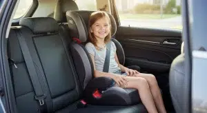 Girl sitting in a booster seat with the car's seat belt low across her thighs and diagonally across her chest