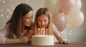 Young girl laughing as she prepares to blow out candles on a birthday cake while her mother smiles beside her