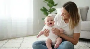 Mother cuddling a smiling baby on a light rug in a bright living room