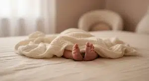 Newborn feet wrapped in a cream muslin blanket in soft window light