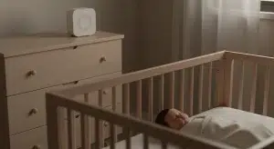 A white noise sound machine on a dresser a safe distance from a crib where a baby sleeps on their back