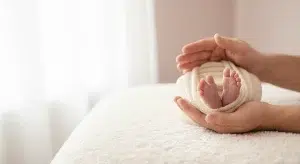 A parent's hands gently cupping a newborn baby's tiny feet on a soft white blanket