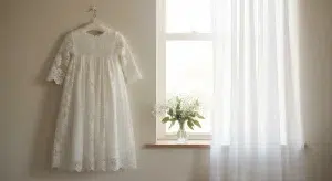 Baptism Bible Verses 25 Kjv Verses for a Babys Baptism | Betteroo A white lace christening gown hanging on a padded hanger beside a sunlit window with sheer curtains