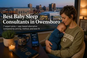 Mother holding a sleeping baby by a window overlooking downtown Owensboro at dusk, baby sleep consultants in Owensboro