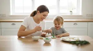 A smiling mother and young son decorating round sugar cookies with icing at a bright kitchen table