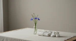 Girl Names That Start with B 141 B Names with Origins and Meanings | Betteroo Blue cornflowers in a glass bottle beside a folded white knit baby cardigan and booties on a pale linen tablecloth