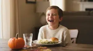 A child laughing at a Thanksgiving dinner table decorated with a small pumpkin and autumn leaves