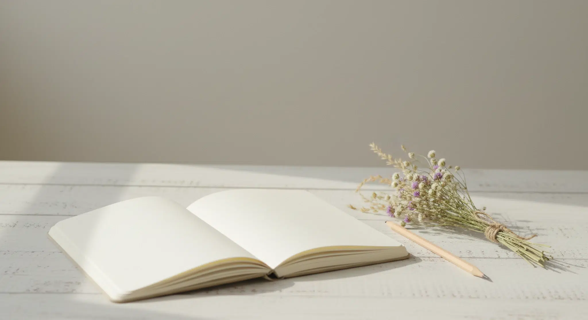 Blank notebook, pencil and a small posy of dried wildflowers on a pale wooden table